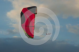 Low angle view of a parafoil and a plane under a cloudy sky during the evening