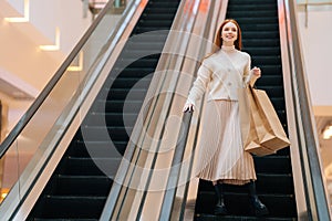 Low-angle view of pretty happy young woman holding on escalator handrail and riding escalator going down in shopping