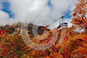 Low angle view of a scenic cable car flying over the colorful autumn valley of Tateyama Kurobe