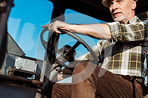 low angle view of senior man in straw hat driving tractor.