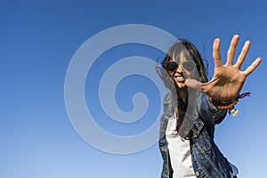 Low angle view of a similing woman while showing the palm of her hand.  Blue sky background.  Copy space. Stop gesture