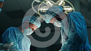 Low-angle view of skilled diverse team of professional doctors operating surgery in dark emergency room. Patient