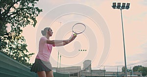 Low angle view in slow-motion of a young female tennis player preparing to serve a tennis match. A woman athlete is