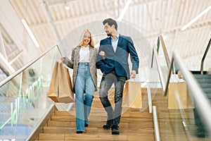 Low-angle view of smiling beautiful young couple holding shopping paper bags with purchases and walking down stairs