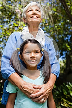 Low angle view of smiling grandmother and granddaughter standing against trees