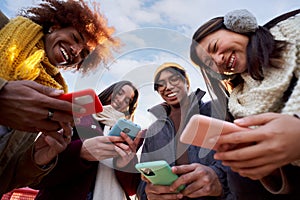 Low angle view of a smiling group of young people using mobile phone. Technology connection addicted