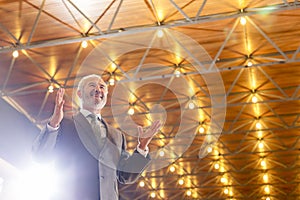 Low angle view of smiling senior businessman in suit gesturing while standing against illuminated roof