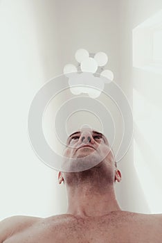 Low angle view of a strong man with naked torso in a white room