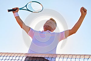 Low angle view of successful man standing with arms raised by tennis net against clear sky