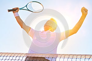 Low angle view of successful man standing with arms raised by tennis net against clear sky