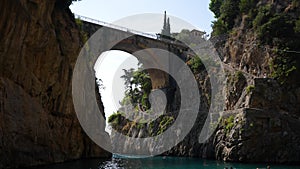 Low-angle view from sunny beach to Fjord Furore Bridge, people relaxing and swimming in Amalfi Coast on summer day