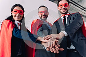 low angle view of super businesspeople in masks and capes putting hands together