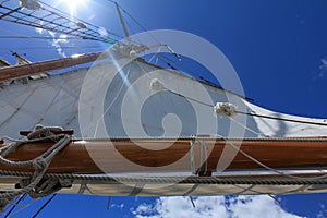 A low angle view of a tall ship sail against a bright blue sky taken looking up from the deck of the boat