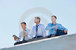 Low angle view of thoughtful mature businessmen sitting and relaxing on rooftop during break in office