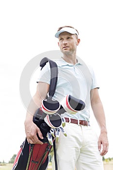 Low angle view of thoughtful mid-adult man carrying golf club bag against clear sky