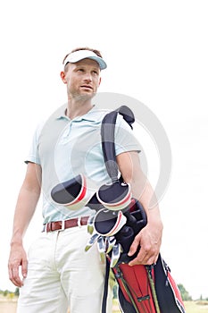 Low angle view of thoughtful mid-adult man carrying golf club bag against clear sky