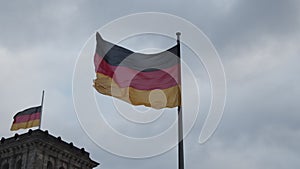 Low angle view of two German national flags waving in wind. Shot against overcast sky at dusk. Berlin, Germany