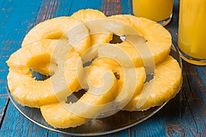 Glasses of pineapple fruit juice and a plate with pieces of pineapple fruit over old wooden background