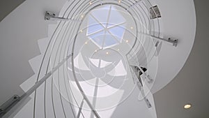 Low angle view of white spiral stairs inside luxury mansion with creative interior design. Daylight coming into house
