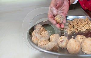 Low angle view of a woman making homemade sweet, coconut laddu for festive season on a domestic table. Close up and selective