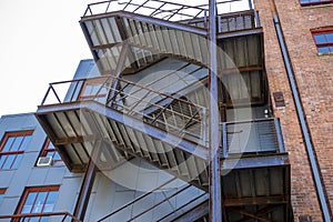 Low angle view of a wooden staircase on the outside of a red brick building, leading to different levels of an apartment or