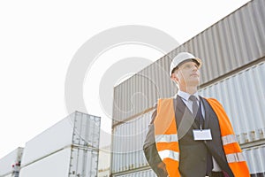 Low angle view of worker standing against cargo containers in shipping yard