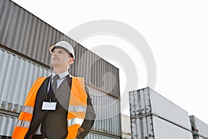 Low angle view of worker standing against cargo containers in shipping yard