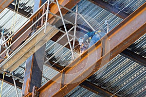 Low-angle view of a worker welding joints on a rusty steel platform at a construction site