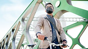 Low angle view of young business man commuter with bicycle going to work outdoors on bridge in city, coronavirus concept