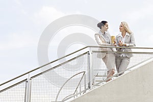 Low angle view of young businesswomen talking while standing by railing against sky