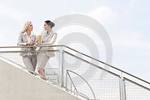 Low angle view of young businesswomen talking while standing by railing against sky