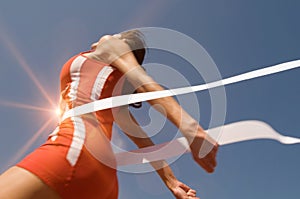 Low angle view of young female athlete crossing finish line against clear blue sky