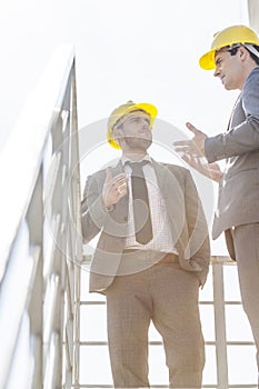 Low angle view of young male businessmen in hard hats having discussion on stairway against clear sky