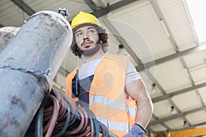 Low angle view of young manual worker moving gas cylinder in metal industry