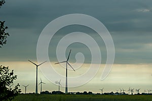 Low-angle of wind turbines in the evening, green meadow and cloudy sky background