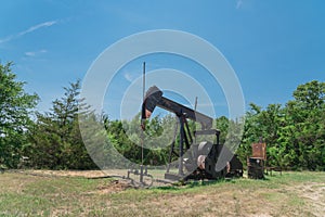 Working pump jack pumping crude oil at oil drilling site in rural USA