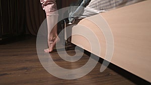 Low angle of a young caucasian woman's legs going down from the bed to the floor. A girl in pejamas comes to the window