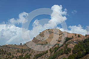 Low angle zoomed in wide shot of a mountain with shed covered roads and cloudy blue sky in the background