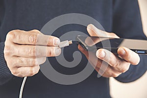 Low battery of smartphone. Male hands holding smartphone and charging with cable line. Cell phone connects plug of charger