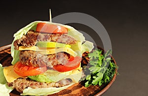 Low carb keto burger without bun wrapped in cabbage leaf with tomatoes, three beef patties, zucchini, cheese, fresh cucumber and h