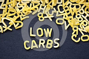 Low carbs phrase spelled with raw letter-shaped pasta on blackboard background