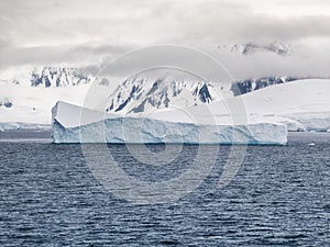 Low clouds and icebergs surrounding the mountainous coastline