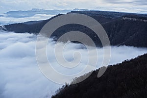 Low clouds, view of winter forest and mountains from observation deck, horizontal picture of amazing natural phenomenon. Beautiful