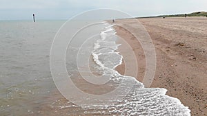 Low drone flying down beach shoreline with water splashing up the sand at a beach in united kingdom