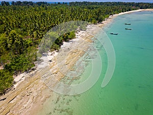 Low drone view of an empty tropical beach surrounded by palm trees (Khao Lak, Thailand