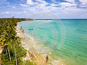 Low drone view of an empty tropical beach surrounded by palm trees (Khao Lak, Thailand