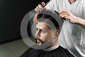 Low fade machine haircut for handsome bearded man in barbershop. Barber with dread locks making hairstyle with a smooth