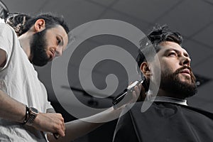 Low fade machine haircut for handsome bearded man in barbershop. Hair cut with a smooth transition.