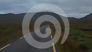 Low flight above narrow road with dashed lines on side. Landscape shot with grasslands and mountains in background