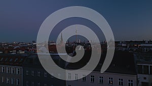 Low flight over building roofs in residential urban borough at dusk. Church tower and Berliner Fernsehturm against sky